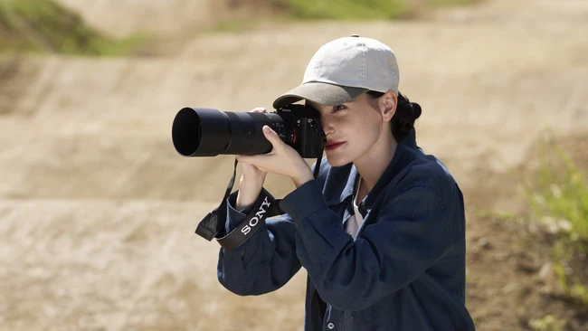 Photographer with camera and telephoto lens wearing cap and navy jacket