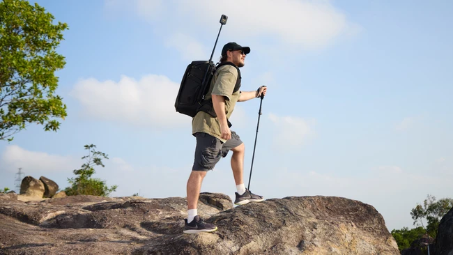 Hiker with backpack and trekking pole standing on rocky terrain against blue sky
