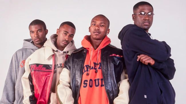 Four men in casual streetwear posed together against a neutral background
