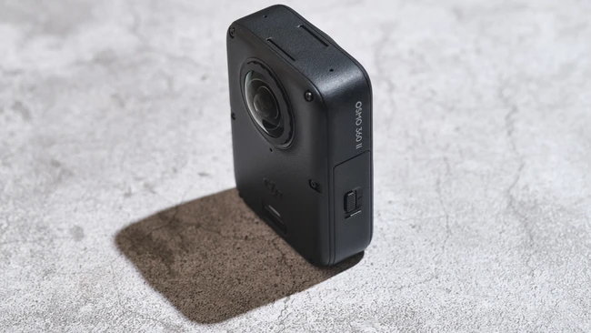 Black compact action camera with lens and side control button on concrete surface