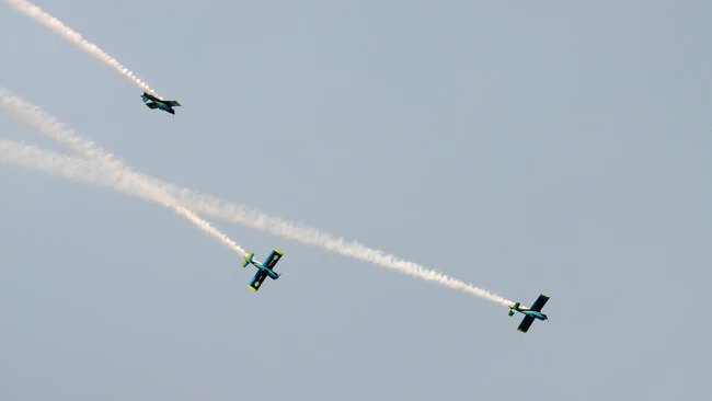 Three aerobatic aircraft in formation flight with smoke trails against a clear sky