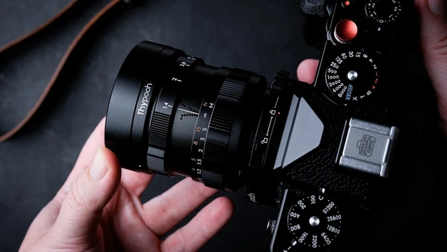Hands holding a vintage rangefinder camera with attached lens, viewed from above