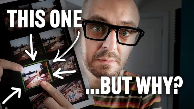 Man with glasses holding multiple printed photographs, pointing at one with a questioning expression