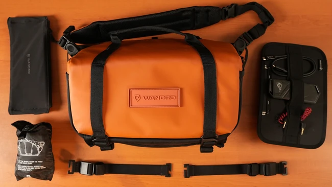 Orange Wandrd camera bag with black straps displayed flat with accessories on orange background