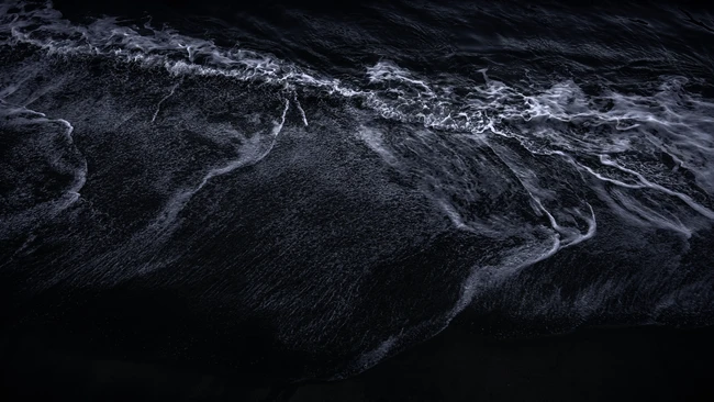 Aerial view of dark ocean water with white wave patterns and foam trails