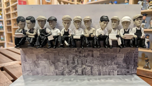 Twelve figurines in vintage work attire standing in a row on a cityscape base