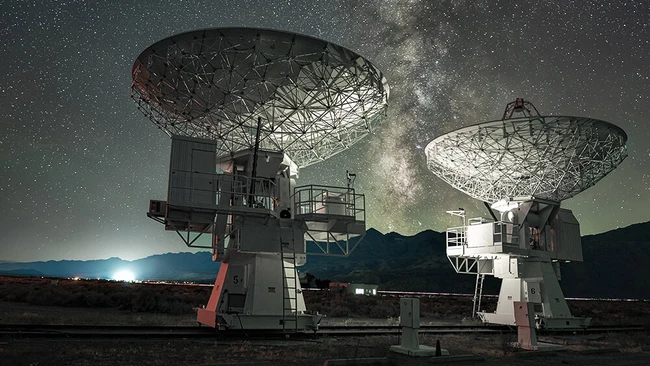 Two large radio telescope dishes pointing skyward beneath the Milky Way at night