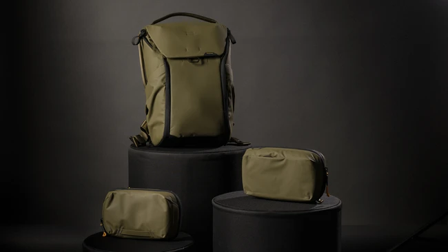 Tan and black camera backpack and modular pouches displayed on black cylindrical pedestals