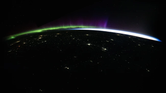 Earth's horizon at night with aurora borealis and city lights from space