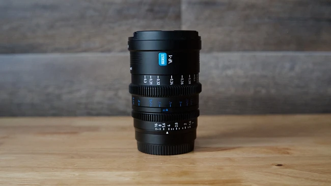 Black manual focus cinema lens with blue markings on wooden surface