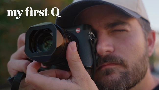 Photographer holding Leica rangefinder camera up to eye while wearing cap