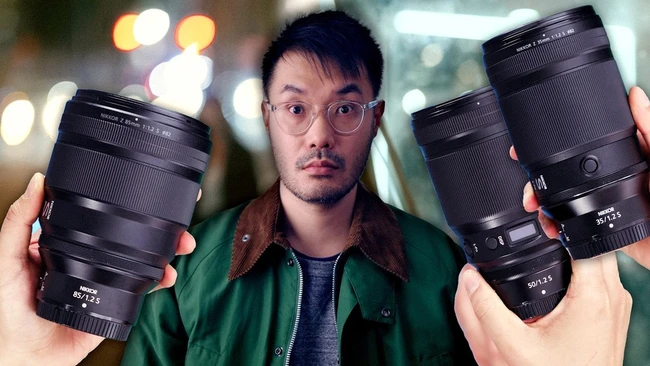 Photographer holding three telephoto lenses while wearing glasses and green jacket