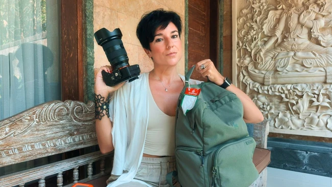 Photographer holding professional DSLR camera and green backpack in ornate interior space