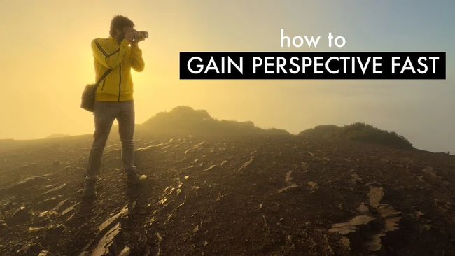 Photographer in yellow jacket standing on rocky terrain at sunrise with mountains in background
