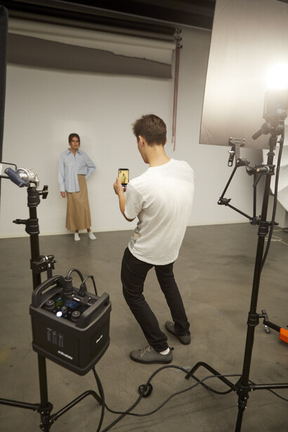 Photographer shooting a portrait of a standing subject in a studio with professional lighting setup.