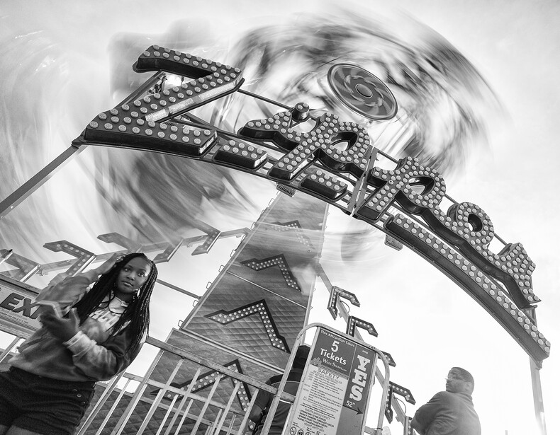 Using the continuous shooting mode with a slow shutter speed caught this moment between the ride operator and the woman in the foreground, with the ride spinning around behind them.