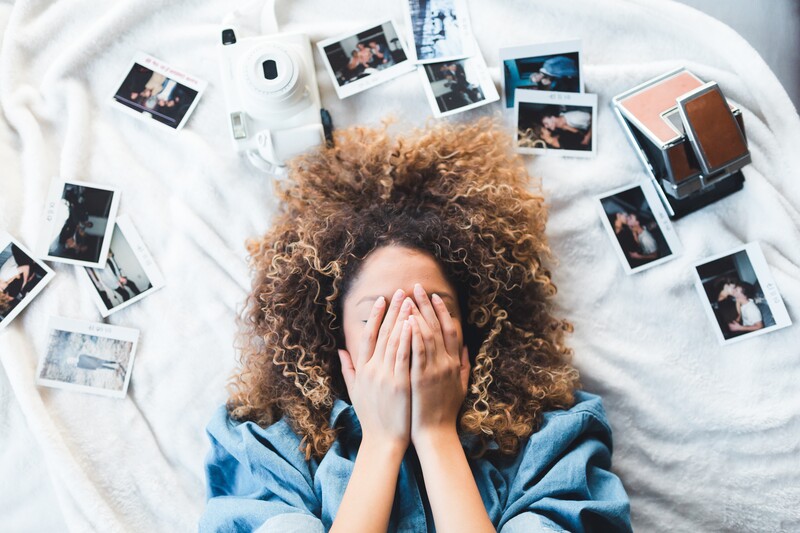 Black female laying on a bed surrounded by Polaroid images.