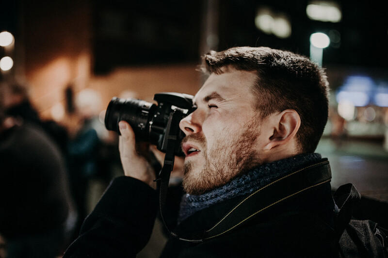 A young man holding a digital camera up to his face.