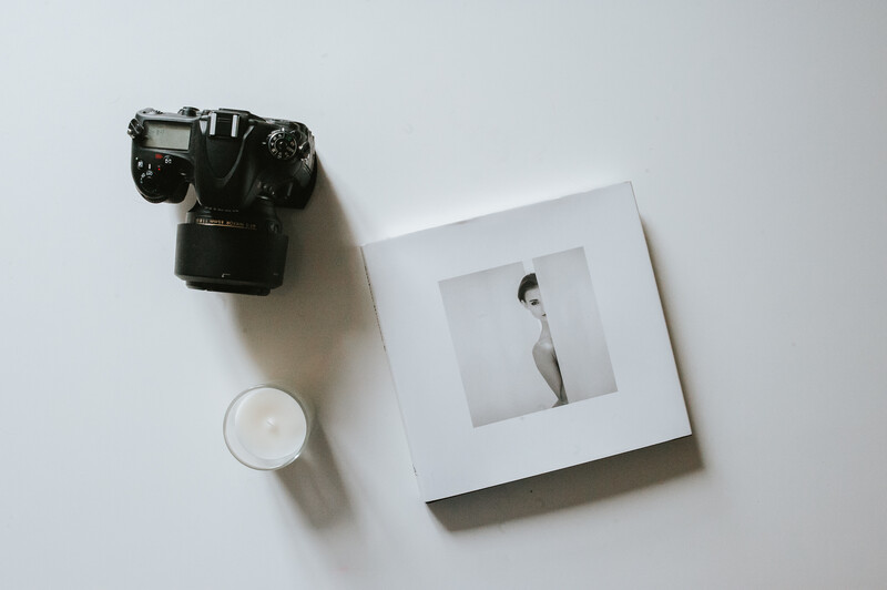 A digital camera, photography book and a candle placed on a white table.