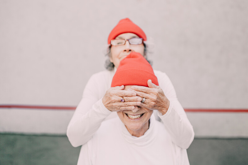 An elderly woman covering friend's face with her hands.