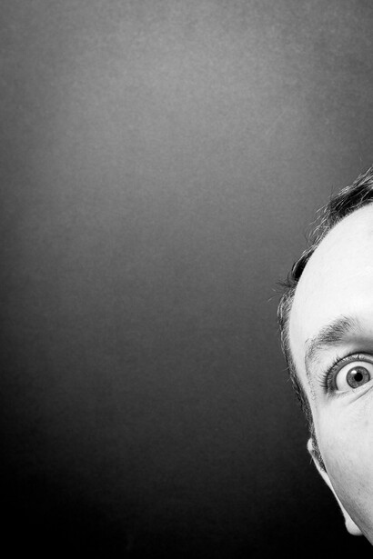 Black and white photo of a startled photographer. Only a portion of the person's head is visible. The person is looking at the camera.