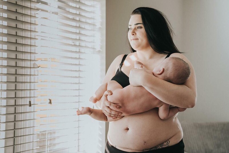 A mother holding her baby by a window.