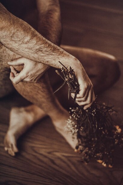 A bare man sat crossed legs, holding a bunch of flowers.