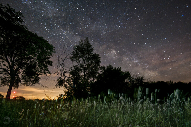 a landscape astrophotograph of a meteor, taken from the top of a hill