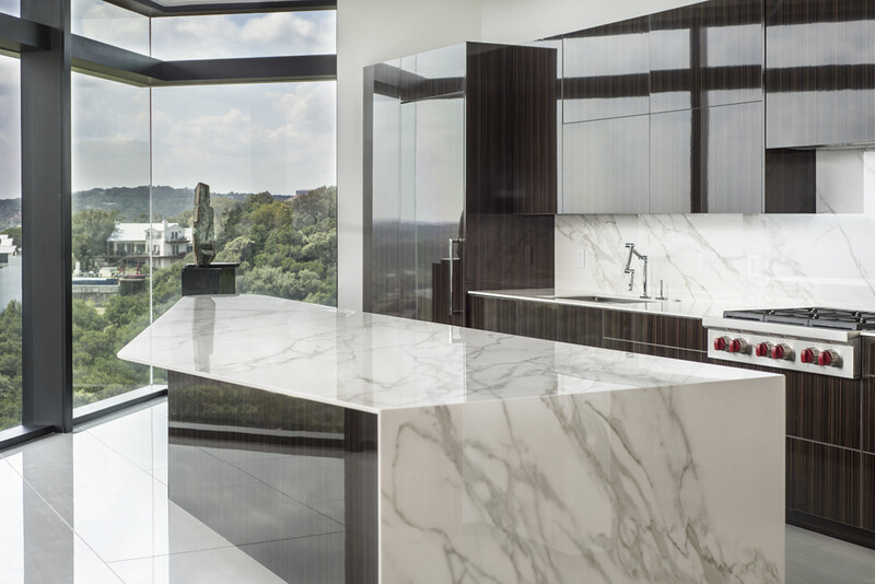 an interior architectural photo showing a stone kitchen island with large bay windows behind it