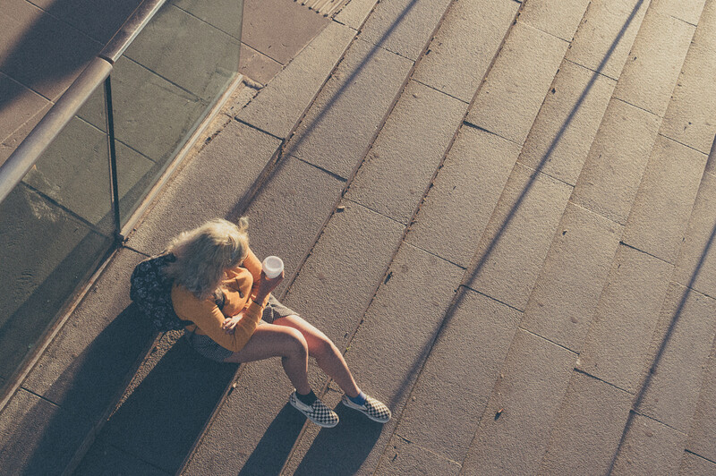 A young blond girl drinking a cup of coffee on a street.