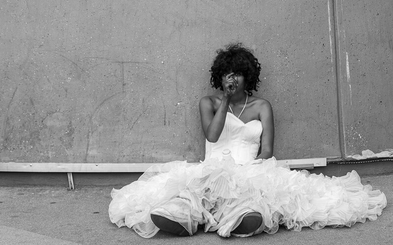 A young woman in a white dress sat on the street.