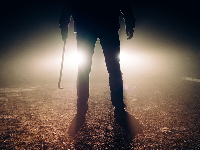a photo of a man backlit by bright truck headlights holding a crowbar