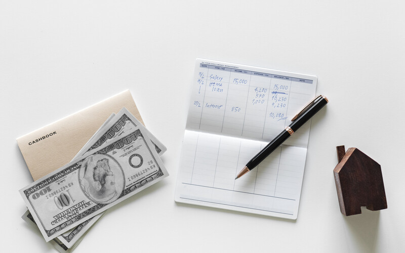 a stock photo of dollar bills, a check ledger and a home figurine