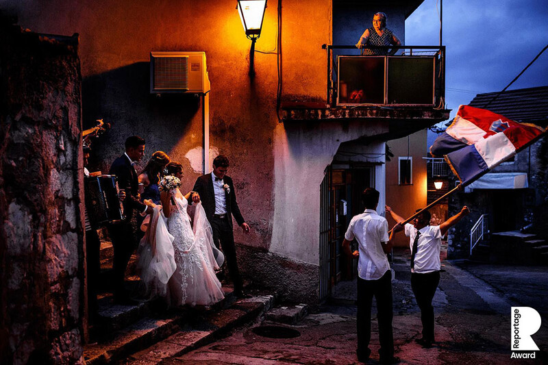 A bride and groom walking through a village.