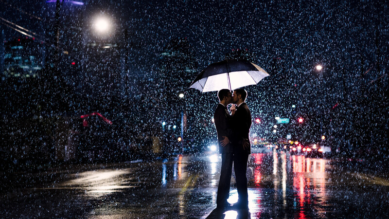Gay couple kissing in the rain while backlit 