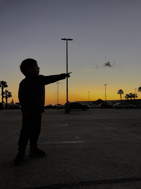 Little boy silhouette pointing at airplane during a sunset