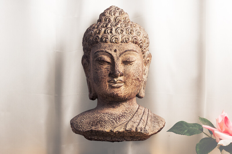 A floating bust of the Buddha in front of a silk curtain with a pink flower and green leaves.