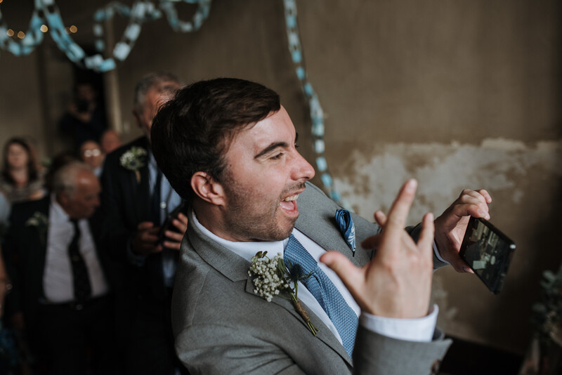 A groomsman taking a phone photograph of the couple