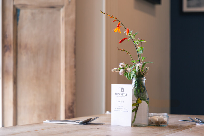 Old wooden cafe table that is laid out with cutlery and flowers.
