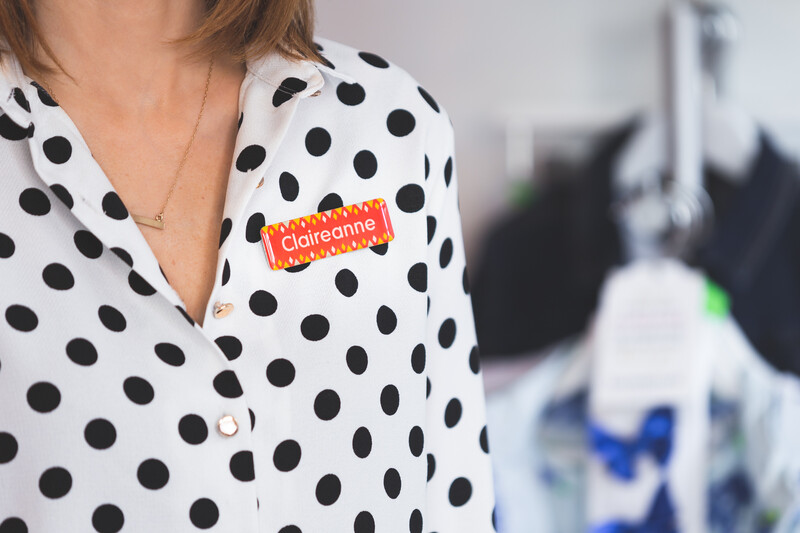 A retail employee wearing a black polka-dot blouse with a name tag