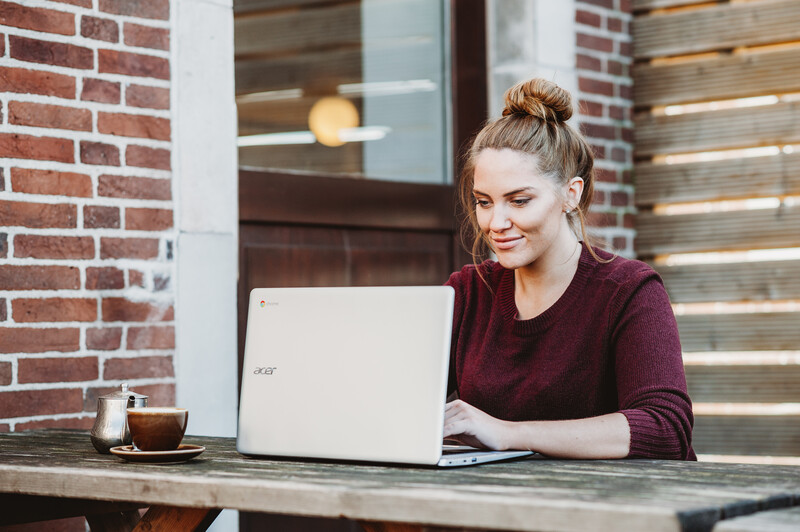A young woman using a laptop at an outdoor cafe table.