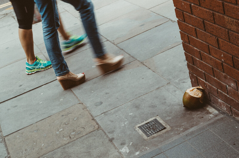Two people walking by an old coconut on the ground