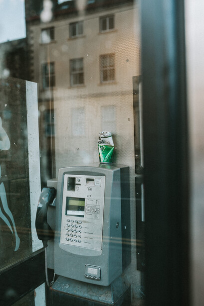 An used beer can on top of a pay phone