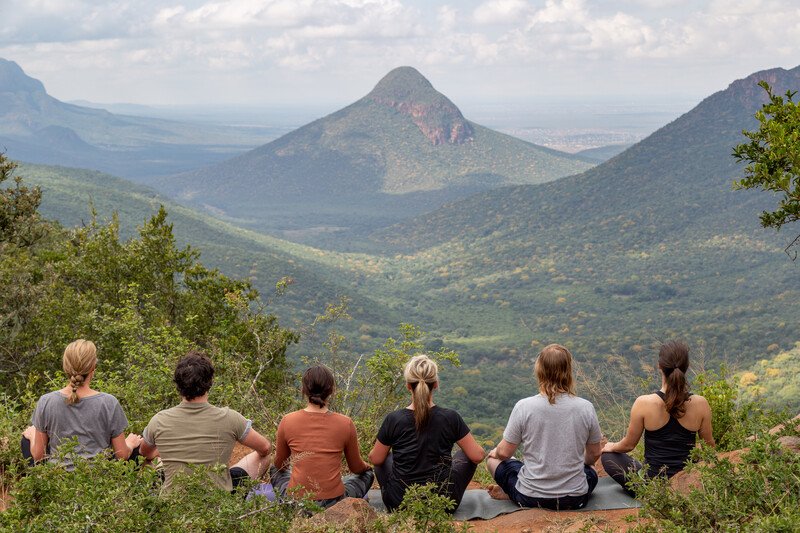 group of people sit meditating overlooking a beautiful vista with a valley and mountains.