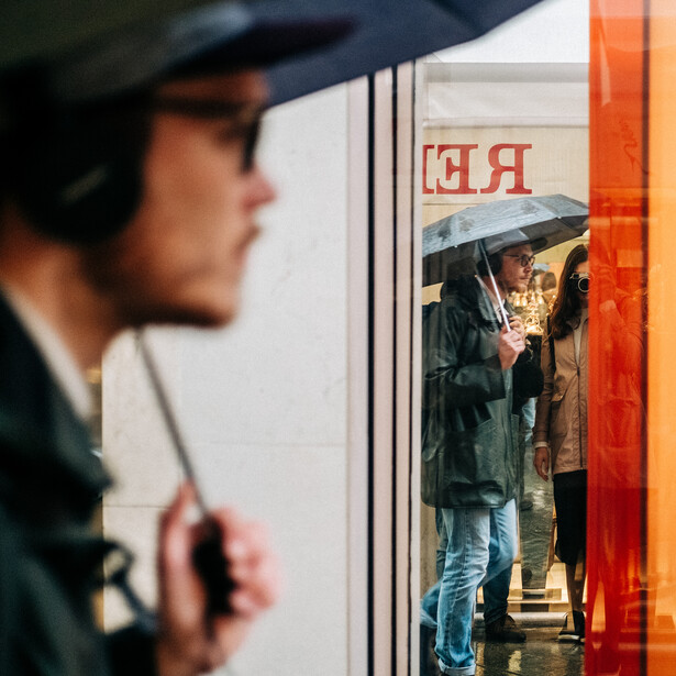 A man with an umbrella walking past a photographer.