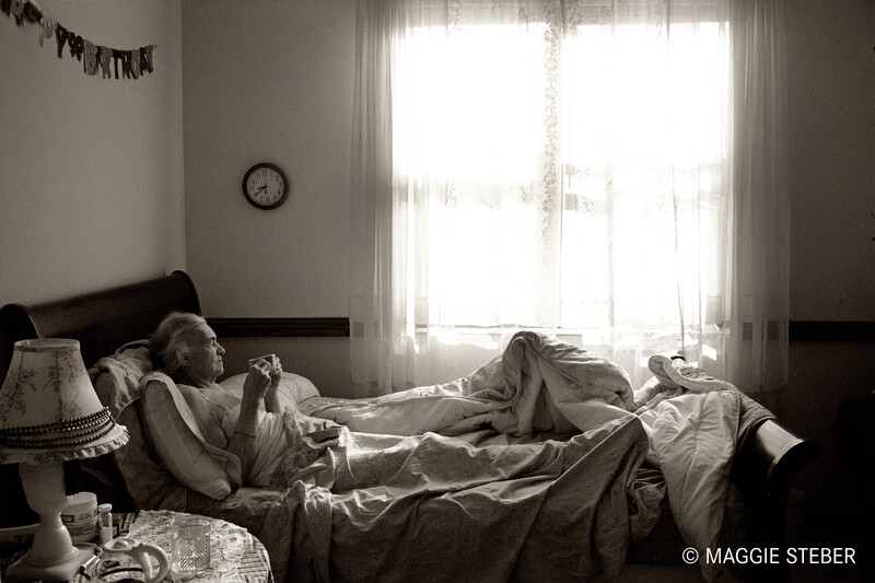 An older woman having a cup of drink in bed.