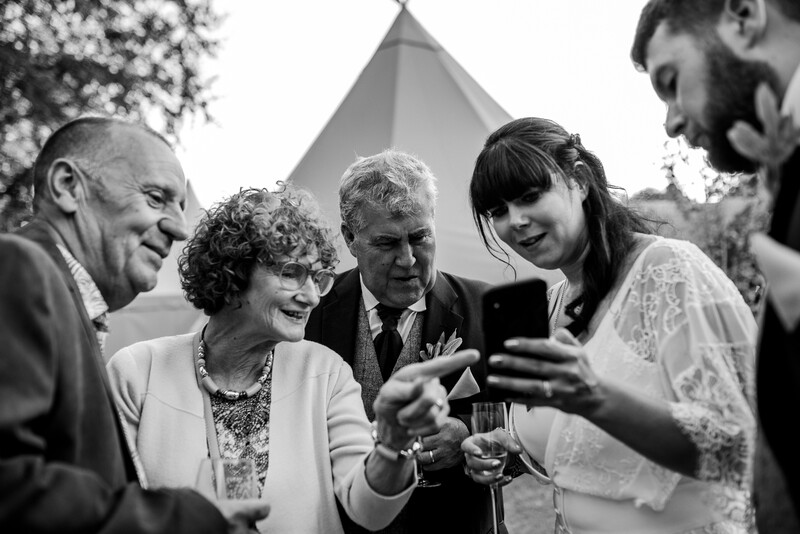 Wedding guests and the bride and groom looking at a phone