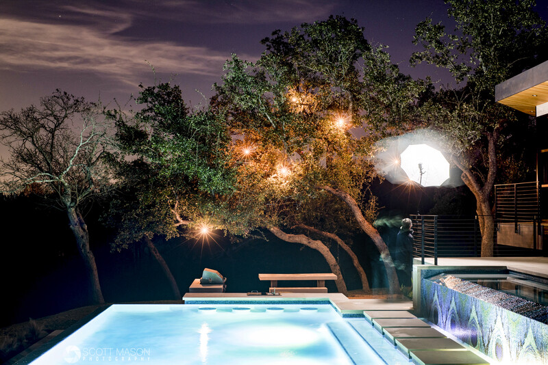 a photographer witha strobe and umbrella lighting trees next to a pool