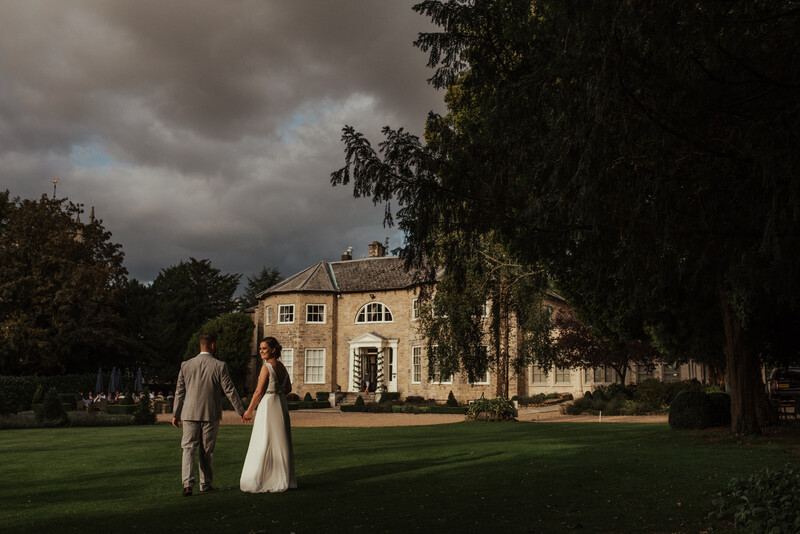 A bride and groom walking in front of a manor. 