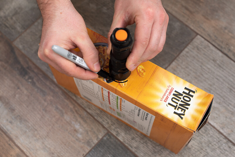 A cereal box is being marked with a permanent marker, prior to cutting